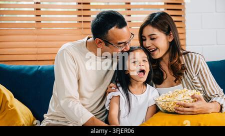 Ein herzerwärmender Familienmoment entfaltet sich, während sie TV und Popcorn auf dem Sofa genießen. Vater, Mutter, Tochter und Geschwister strahlen Glück aus und schaffen geschätzte Erinnerungen Stockfoto