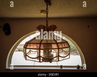 Vintage Pendelleuchte aus buntem Glas, die vor einem halbrunden Fenster in einem Retro-Innenraum hängt Stockfoto