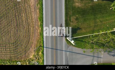 Luftaufnahme von oben: Pferd und Kutsche. Amish-Menschen aus Pennsylvania fahren auf einer ländlichen Straße. Das helle Licht der Goldenen Stunde wirft einen langen Schatten von Pferd und Kutsche Stockfoto