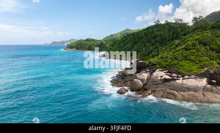 Wellen schlagen gegen schroffe Felsen, eingerahmt von dichter, grüner tropischer Vegetation. Seychellen, Mahe. Stockfoto