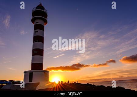 Der Leuchtturm von Punta Sardina erhebt sich vor einem tiefblauen Abendhimmel, mit einem langen, leuchtenden Wolkenschwanz, der sich über den Horizont erstreckt bei Sonnenuntergang auf Gran C Stockfoto