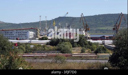 Betriebsamer Industriehafen, der große Windturbinengläser und Frachtcontainer abfertigt, und dabei die globale Lieferkette für erneuerbare Energien und maritime Logistik präsentiert. Stockfoto