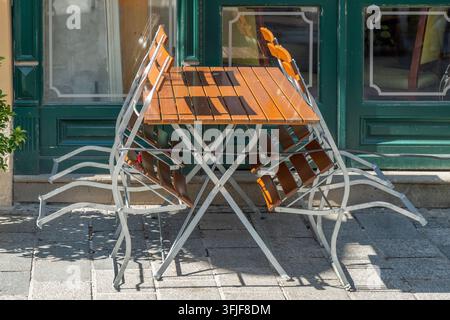 Ein leerer Außentisch mit gefalteten Stühlen steht vor einem grünen Laden. Stockfoto