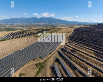 Sonnenkollektoren füllen trockene Hügel Felder unter klarem Himmel. Diese Solarfarm erstreckt sich über Reihen von Photovoltaik-Arrays, mit einer Bergkette in der Ferne Stockfoto