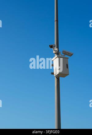 Überwachungskameras und Sicherheitsausrüstung, die an einem Strommast montiert sind, vor einem blauen Himmel, stellvertretend für Videophone, städtische Sicherheit und moderne Infrastruktur Stockfoto