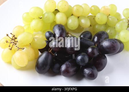 Frische grüne und dunkelvioletten Traubenbeeren ruhen auf einer weißen Tellerfläche Stockfoto