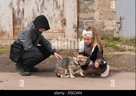 Fürsorglicher Junge und Mädchen streicheln süßen Hund in der Nähe alter Garagentore. Empathie gegenüber Straßentieren. Kinder genießen süßen Mischlingshund. Fürsorge für den Hund. soc Stockfoto