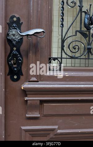 Nahaufnahme einer dunkelbraunen, panelierten Holztür mit einem verzierten Metallgriff, einem Schlüsselloch-Schild und einem dekorativen schmiedeeisernen Fenstergitter. Die Deta Stockfoto