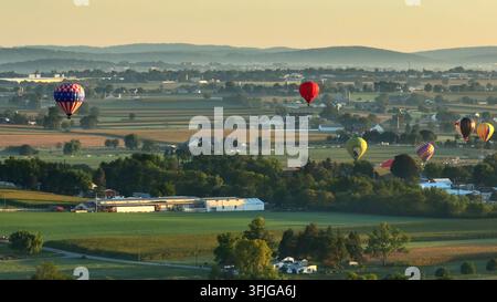 Luftbild zeigt eine Gruppe von Heißluftballonen, die über einer malerischen Landschaft in Amerika während eines Heißluftballonfestivals zur Sonnenuntergangzeit fliegen, East Lampeter Zu Stockfoto