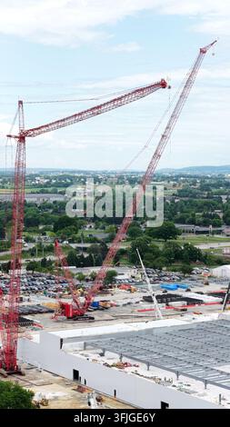 Rote Turmkrane erheben sich über einer Rechenzentrum-Baustelle in der Nähe von Lancaster, Pennsylvania, Arbeiter bauen ein großes Lagerhausdach neben einem überfüllten Parkplatz a Stockfoto