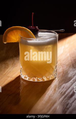 Schöner Whiskey Sour auf Eis garniert mit einer Orangenscheibe und einer dunklen Kirsche Stockfoto