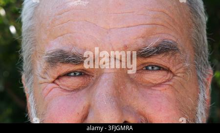 Blaue Augen älterer Männer, die blinzeln und in die Kamera im Freien schauen. Faltiges Gesicht eines älteren Menschen mit traurigem Anblick. Gestörter Gesichtsausdruck von Stockfoto