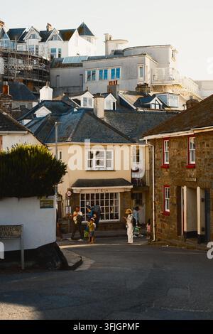 Saint Ives, Cornwall – 6. August 2026: Familien schlendern eine gepflasterte Straße entlang, umgeben von traditionellen Küstenhäusern. Stockfoto