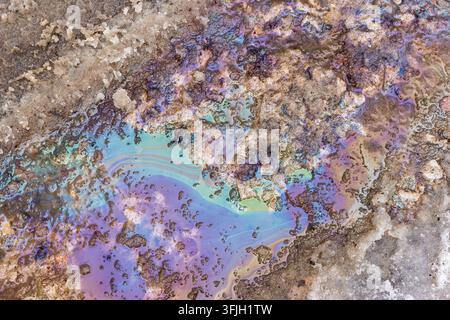 Irideszenter Ölteppichfilm, der im schmelzenden schmutzigen Schnee schimmert, Straßenverschmutzung im Frühling mit Regenbogenfarbenen chemischen Flecken, gefährlicher Kraftstoffaustritt auf eisigem Boden Stockfoto