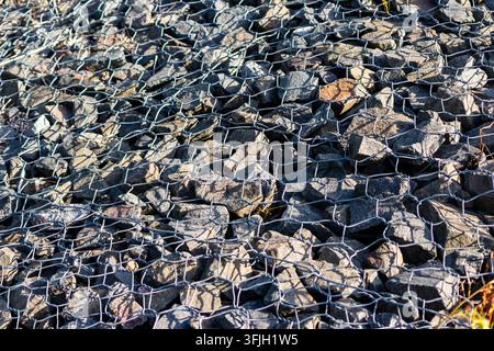 Detaillierte Nahaufnahme einer robusten Gabionenstruktur aus Schotter, eingeschlossen in einem haltbaren Metallmaschengewebe, das zur Ufererosionskontrolle und Boden verwendet wird Stockfoto