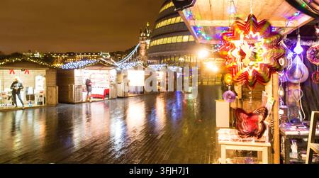 Menschen durchstöbern Weihnachtsstände am More London Riverside und feiern die Feiertagszeit in der Nähe des Rathaus und der Tower Bridge. Stockfoto