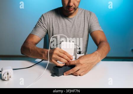 Nahaufnahme von männlichen Händen, die viele Kabel und Stecker in einem Verlängerungskabel handhaben. Szene stellt technologische Abhängigkeit, Strombedarf, Organisation und Unordnung dar Stockfoto