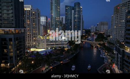 Boote auf dem Fluss in der Innenstadt von Fort Lauderdale bei Nacht. Moderne Wohnkomplex-Türme und Wolkenkratzer leuchten am Abend. Aufsteigendes Drohnen-Breitbild Stockfoto
