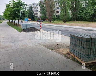 Städtsche Straßenszene, die Straßenbau- oder Instandhaltungsarbeiten in einem Wohngebiet zeigt. Im Vordergrund befinden sich Paletten mit grauen Betonpflastersteinen Stockfoto