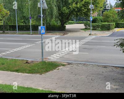 Eine urbane Straßenszene im Freien mit einem Zebrastreifen an einer Asphaltstraße. Im Vordergrund ein blaues quadratisches Verkehrsschild mit einem Stockfoto