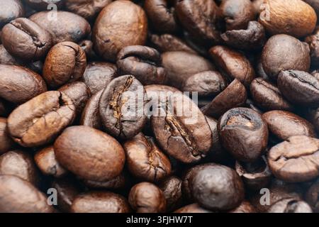 Nahaufnahme der Textur gerösteter Kaffeebohnen, die das Bild ausfüllen, reiche braune Makroaufnahme mit sichtbaren Rissen, Ölschimmer und Schatten im Fokus Stockfoto