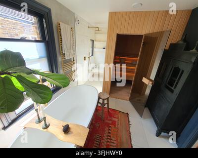 Ein geräumiges, modernes Luxus-Badezimmer-Interieur mit einer freistehenden weißen ovalen Badewanne und einem natürlichen hölzernen Badekorb, der zwei Kerzen und ein Stockfoto