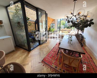 Modernes Wohn- und Esszimmer im offenen Grundriss mit großen schwarz gerahmten Falttüren aus Glas, die zu einem kleinen privaten Innenhof mit freiliegendem Stockfoto