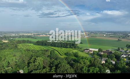 Luftbild von ländlichem Pennsylvania, das üppige grüne Felder und sanfte Hügel unter einem weiten Himmel zeigt. Ein lebendiger Regenbogen wölbt sich über die Landschaft und verleiht einen Hauch von Stockfoto