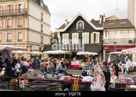Einkäufer durchstöbern Freiluftstände auf dem Sonntagmarkt Garibaldi in Saint-Ouen, Frankreich, bei der Paul-Bäckerei, um Kleidung und Waren zu kaufen. Stockfoto
