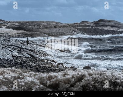 Wellen schlagen gegen die felsige Küste unter dem Himmel. Die Szene fängt die Küste mit einem Infrarotfilter ein und zeigt ein einzigartiges Lichtspektrum. Stockfoto
