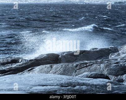 Wellen schlagen gegen die felsige Küste, aufgenommen im nahen Infrarot-Spektrum. Die Szene zeigt spritzendes Wasser und einzigartige Texturen auf den Felsen entlang der Küste. Stockfoto