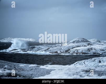 Eine Küste mit Felsen und vereisten Stellen. Wellen schlagen gegen das Ufer, während die Landschaft im Infrarot erscheint. Die Atmosphäre wirkt kalt und distanziert. Stockfoto
