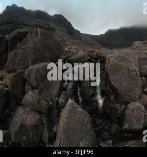 Ein Gebirgsbach stürzt über Geröll unter den schroffen Cuillin-Gipfeln auf der Isle of Skye, Schottland. Stockfoto
