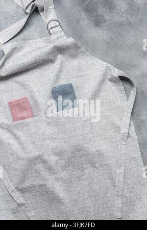 Graue Küchenschürze im Nahaufnahme mit Servietten in der Tasche. Grauer Betonhintergrund. Oberansicht, Flat Lay. Stockfoto