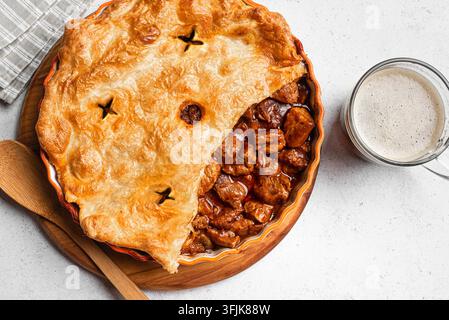 Rindfleisch-Pastete mit dunkler Biersauce und knusprigem Blätterteigboden auf weißem Hintergrund, Ansicht von oben. Hausgemachtes Fleischbier-Pastetenrezept. Stockfoto