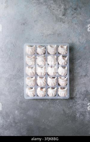 Tiefgekühlte Fertiggerichte asiatischen potstickers Klöße zu kochen von Garnelen in Kunststoffbox über grau Textur Hintergrund gefüllt. Ansicht von oben, Platz. Halbzeug Stockfoto
