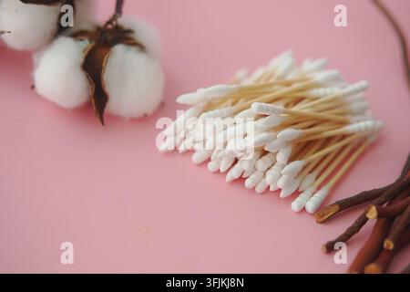 Sortiment an Wattebällchen und Wattestäbchen, die auf einer rosa Oberfläche ausgelegt sind Stockfoto
