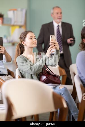 Junge Studentin verwendet Smartphone oder Tablet, um QR-Codes zu scannen oder Fotos im Hörsaal zu machen Stockfoto