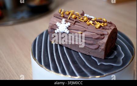 Traditioneller weihnachtlicher Schokoladen-Yule-Log-Kuchen auf einem dekorativen schwarz-weißen Keramikteller. Buche de Noel festliches Feiertagsdessert mit reicher Schokoladenfüllung Stockfoto