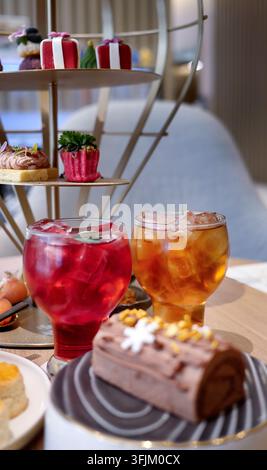 Festliches Nachmittagsteeset, das auf einem Holztisch in einem eleganten Café serviert wird. Zwei erfrischende Eiskaltgetränke in runden Gläsern, die neben traditioneller Schokoladenjul nebenstehen Stockfoto