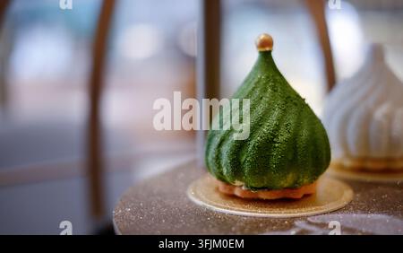 Nahaufnahme eines Gourmet-Grün-Mousse-Kuchens in Form eines modernen Weihnachtsbaums. Elegantes festliches Feiertagsdessert mit samtiger Textur, grüner Glasur und Goldperlen-Dekor Stockfoto