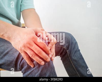 Männliches Knie verletzt. Wunde Stelle, die durch einen roten Marker hervorgehoben wird. Der Mann berührt sein Bein mit den Händen. Nahaufnahme auf weißem Hintergrund. Knochenschmerzen oder Knie um das Knie Stockfoto