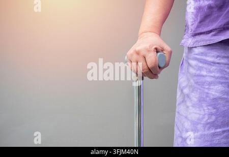 Nahaufnahme einer asiatischen Seniorin, die einen Gehstock hält, mit hellgrauem Hintergrund und Platz für einen Text. Gehstock zu Hause Konzept Stockfoto