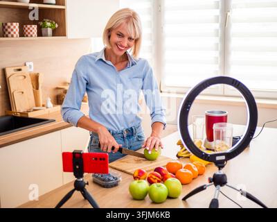 Home-Cooking-Influencer bereitet frische Zutaten vor einer Smartphone-Kamera und einem professionellen Ringlicht vor. Stockfoto