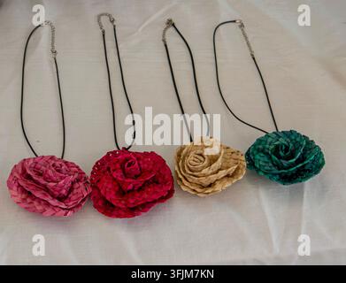 Vier geflochtene Strohblumen-Anhänger in Rosé-, Rot-, Naturbraun- und Türkistönen hängen an schwarzen Schnüren. Sie sind nebeneinander in einem einfachen Muster angeordnet Stockfoto