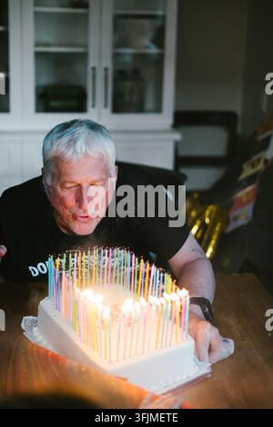 Senior Mann bläst viele Geburtstagskerzen auf einem Kuchen aus Stockfoto