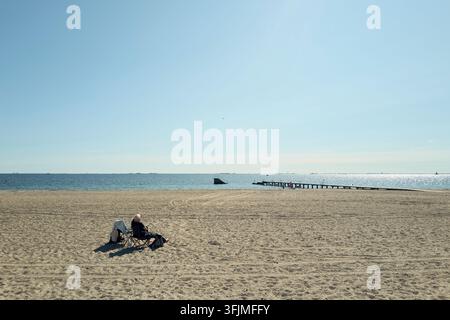 Ältere Person sitzt allein an einem sonnigen Strand Stockfoto