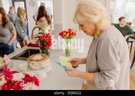 Seniorin liest eine Grußkarte zu Hause mit der Familie Stockfoto