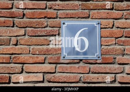 Blaues Hausnummer Sechs Schild an einer verwitterten roten Backsteinwand montiert Stockfoto