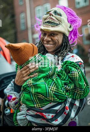 Lächelnde Frau in grusligem Clownskostüm hält ein Baby Stockfoto